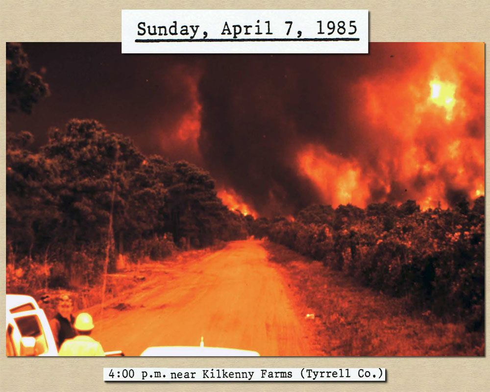 April 7, 1985 4:00 pm: Photo of flames near Kilkenny Farms, smoke so thick sky as dark
				   as night